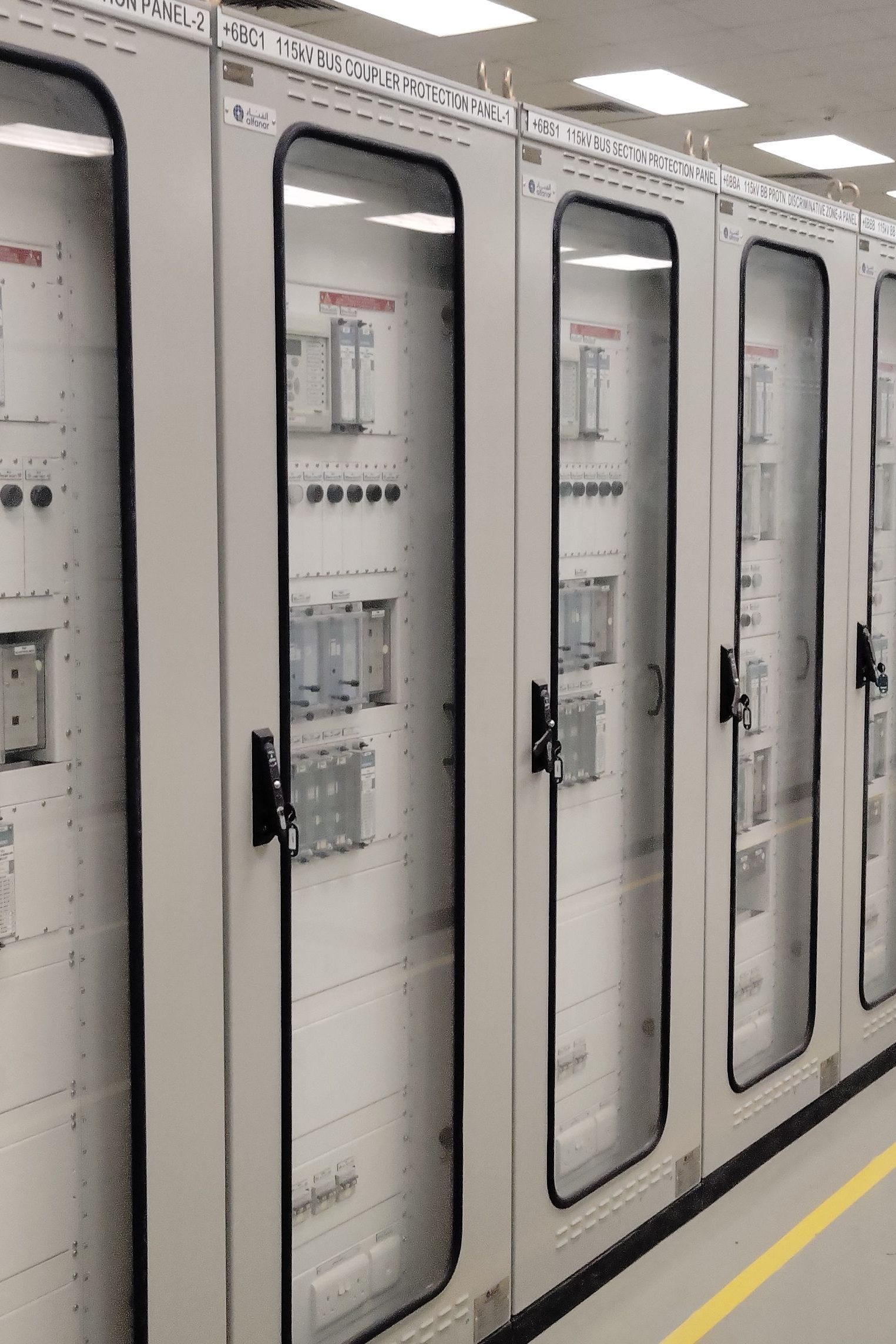 View of an industrial control room featuring rows of electrical panels in a well-lit environment.